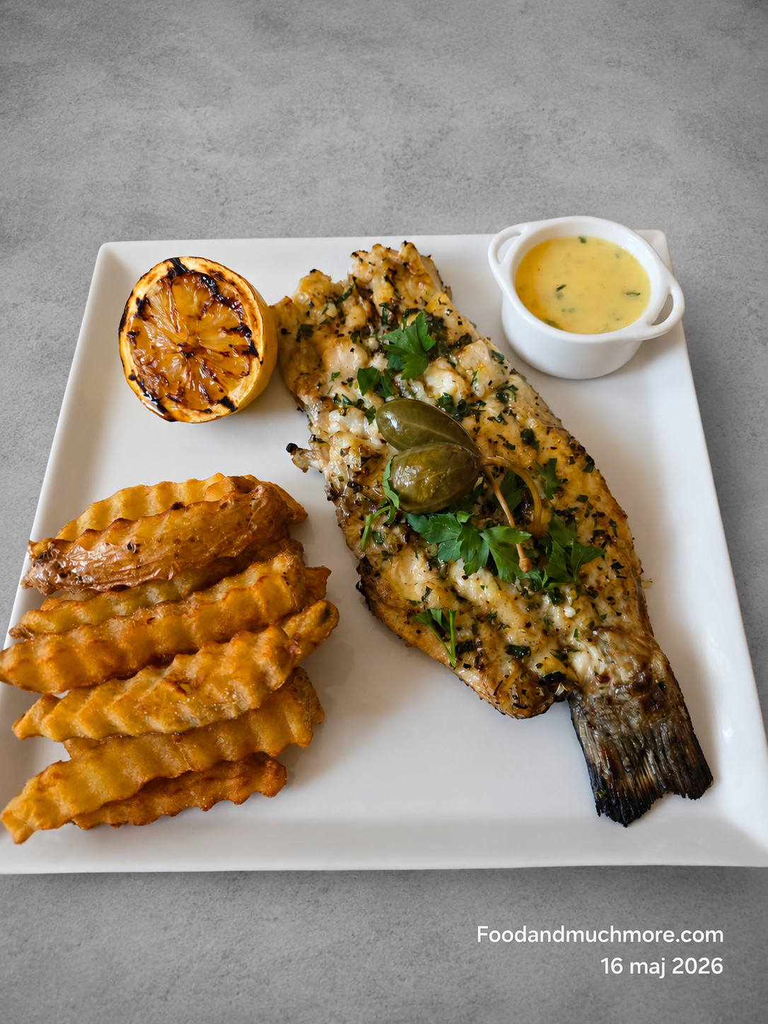 Grillad sea bass med hemmagjorda pommes, grillad citron och Beurre Blanc på vit tallrik mot grå bakgrund.
