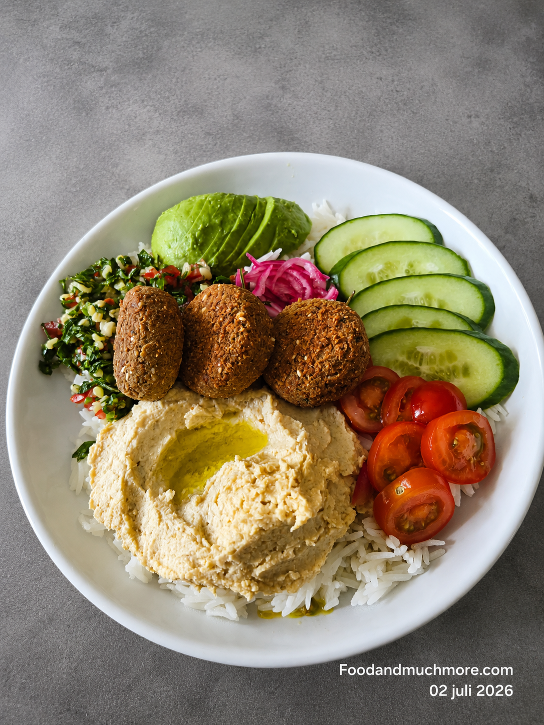 Krispig Falafel Bowl Deluxe med hemmagjord falafel, hummus, tabbouleh, picklad rödlök, avokado, granatäpple och tahinidressing serverad i en skål.