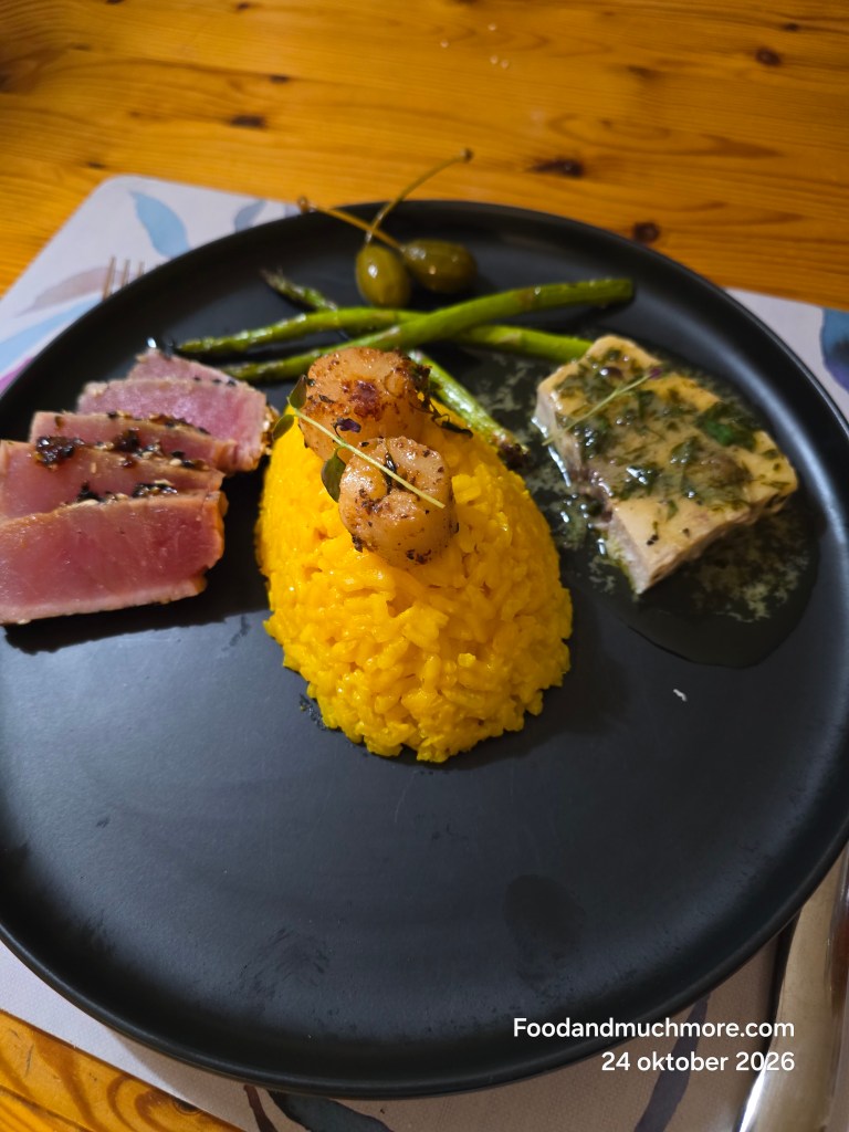 Sesamstekt tonfisk och siciliansk svärdfisk med saffransrisotto, pilgrimsmusslor, citronsmörsås och grön sparris på svart tallrik.